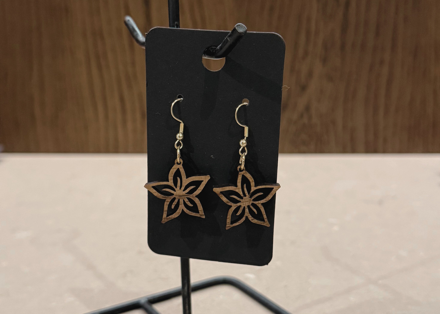 Pair of wood starflower-shaped earrings on a black card against a wooden background
