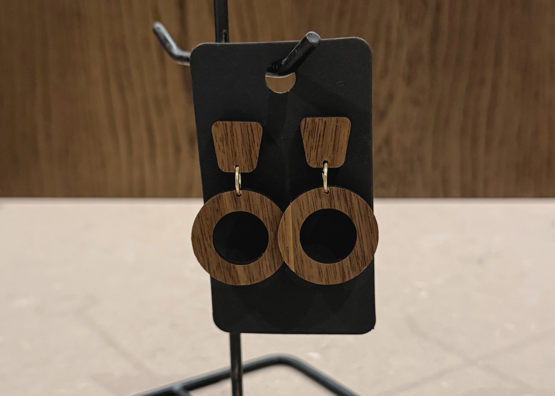 Wooden earrings on a black earring stand against a wooden background